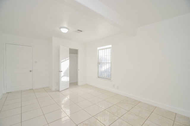 empty room with beam ceiling and light tile patterned floors