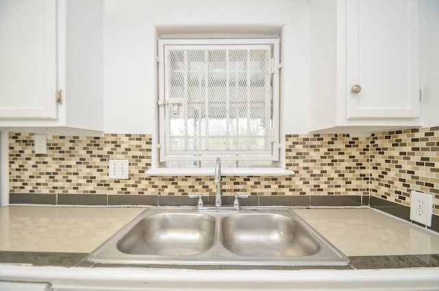 interior details with backsplash, white cabinetry, and sink