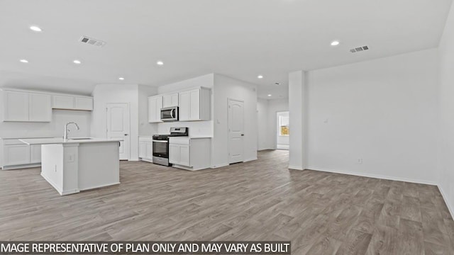 kitchen with light wood-type flooring, stainless steel appliances, sink, a center island with sink, and white cabinetry