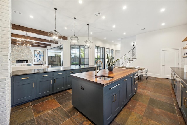 kitchen with sink, blue cabinetry, beamed ceiling, hanging light fixtures, and an island with sink