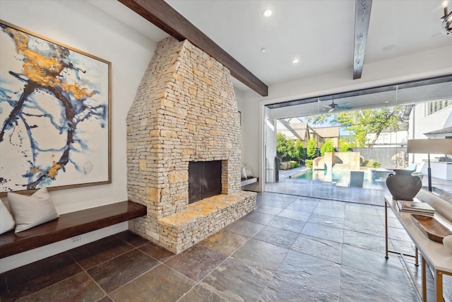 living room featuring beamed ceiling, ceiling fan, and a stone fireplace