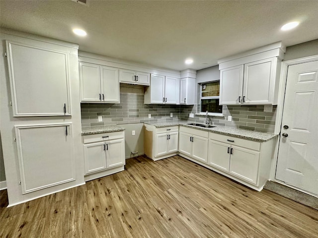 kitchen featuring decorative backsplash, white cabinets, light hardwood / wood-style floors, and light stone counters