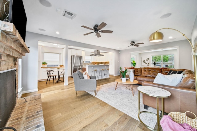 living room featuring a brick fireplace, ceiling fan, and light hardwood / wood-style flooring