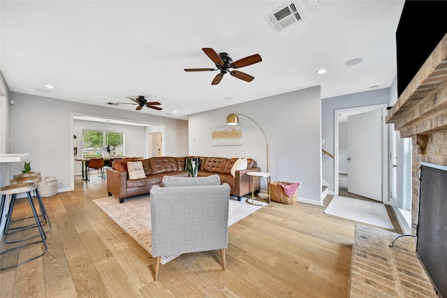 living room with ceiling fan, light hardwood / wood-style floors, and a brick fireplace