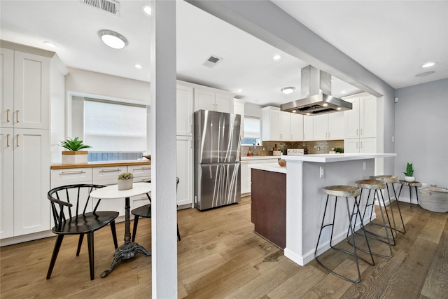 kitchen with white cabinets, a wealth of natural light, island exhaust hood, and stainless steel refrigerator