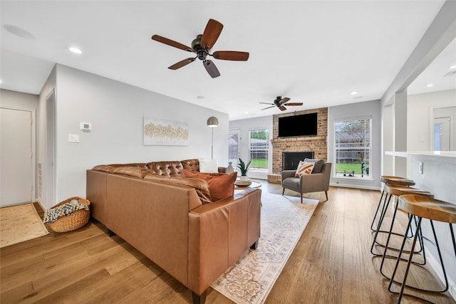 living room featuring light wood-type flooring, a brick fireplace, and ceiling fan