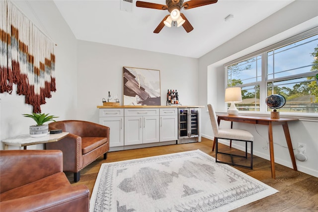 office space with ceiling fan, light hardwood / wood-style floors, wine cooler, and bar area