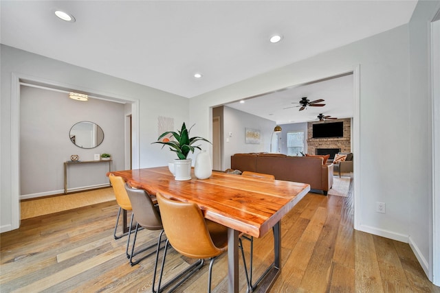 dining room featuring ceiling fan, light hardwood / wood-style flooring, and a brick fireplace