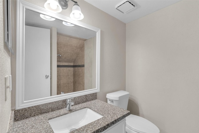 bathroom with a tile shower, vanity, and toilet