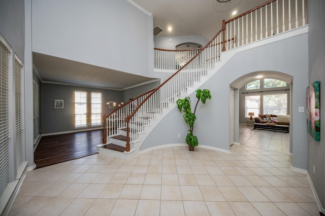 foyer featuring crown molding, a towering ceiling, and light tile patterned flooring