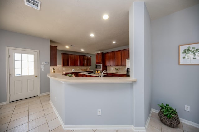 kitchen featuring kitchen peninsula, decorative backsplash, stainless steel microwave, and light tile patterned floors