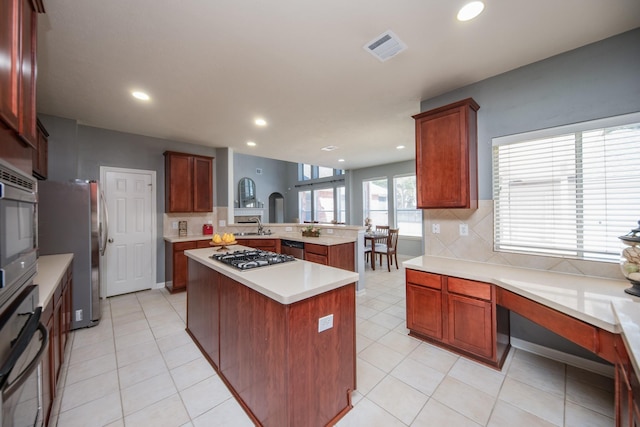 kitchen featuring a center island, light tile patterned floors, appliances with stainless steel finishes, tasteful backsplash, and kitchen peninsula