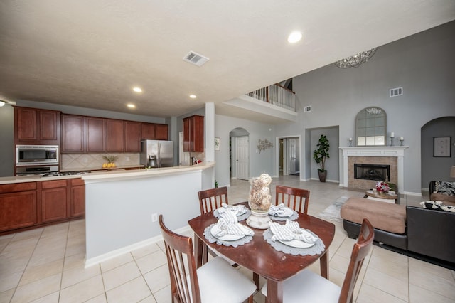 dining space featuring a fireplace, light tile patterned floors, a towering ceiling, and a chandelier