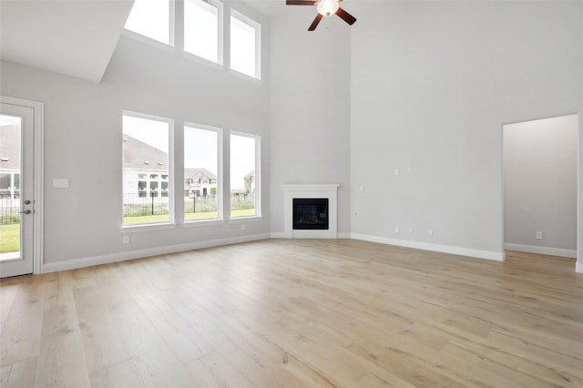 unfurnished living room with ceiling fan, light hardwood / wood-style floors, and a high ceiling