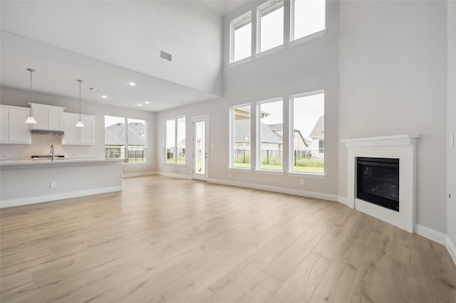 unfurnished living room featuring a high ceiling, light wood-type flooring, a wealth of natural light, and sink