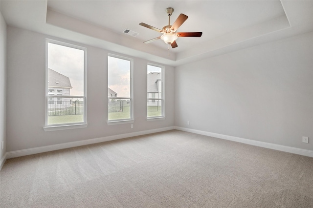 carpeted spare room with a raised ceiling and ceiling fan