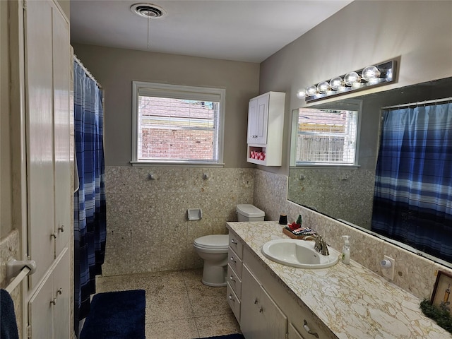 full bath featuring visible vents, wainscoting, toilet, vanity, and tile walls