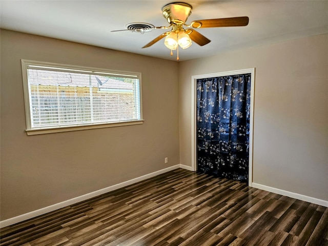 empty room with dark wood-style floors, ceiling fan, and baseboards