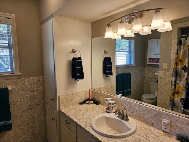 bathroom featuring wainscoting, vanity, toilet, and tile walls