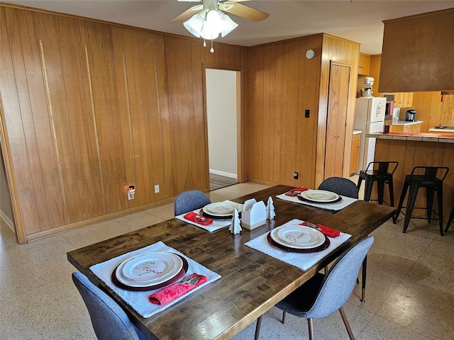 dining space with ceiling fan and wooden walls