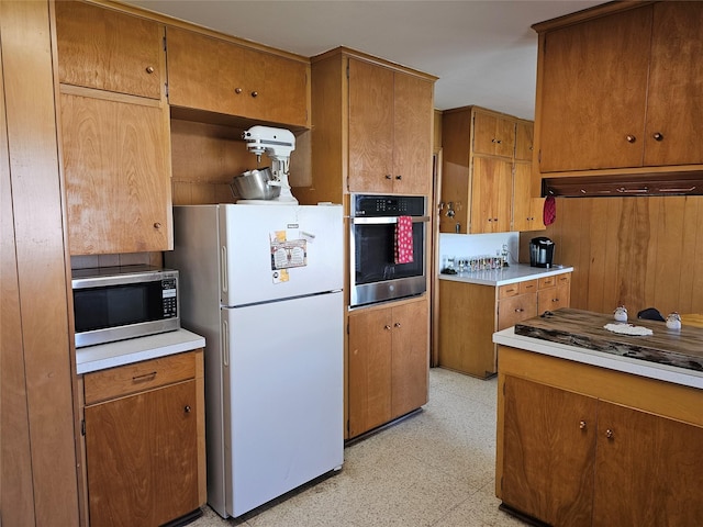 kitchen featuring brown cabinets, light floors, under cabinet range hood, and stainless steel appliances