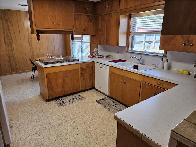 kitchen featuring kitchen peninsula, white dishwasher, stainless steel gas cooktop, wooden walls, and sink