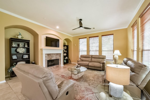 tiled living room with a fireplace, built in features, ceiling fan, and crown molding