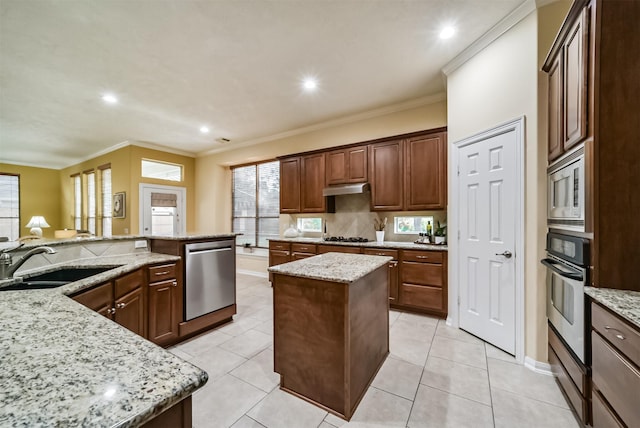 kitchen with light stone countertops, sink, appliances with stainless steel finishes, a kitchen island, and ornamental molding