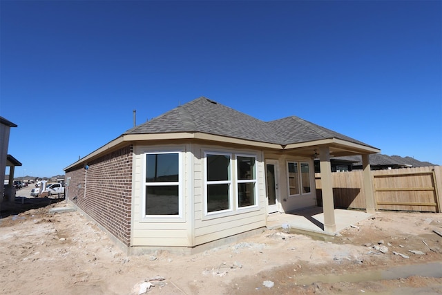 back of house featuring brick siding, roof with shingles, a patio, and fence