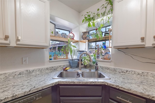 kitchen featuring white cabinets, light stone counters, stainless steel dishwasher, and sink