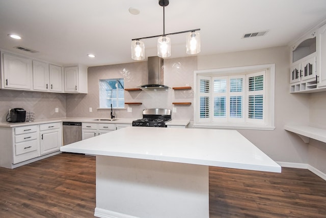 kitchen featuring sink, wall chimney exhaust hood, stainless steel appliances, decorative light fixtures, and white cabinets