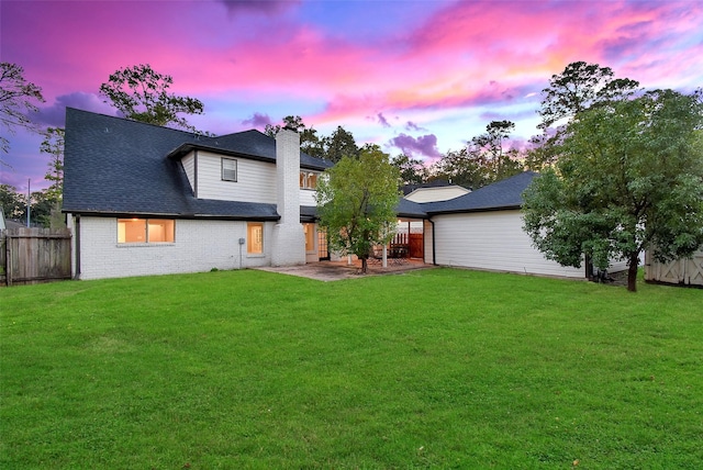 back house at dusk featuring a patio area and a yard