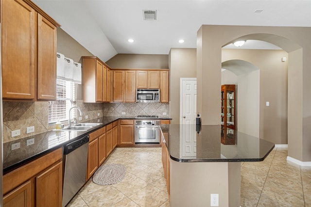 kitchen with sink, tasteful backsplash, a center island, dark stone countertops, and appliances with stainless steel finishes