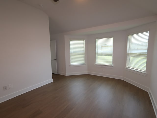 spare room featuring dark wood-style flooring, baseboards, and vaulted ceiling