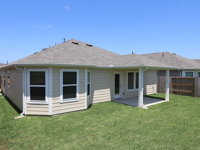 rear view of property with a lawn, fence, a shingled roof, and a patio area