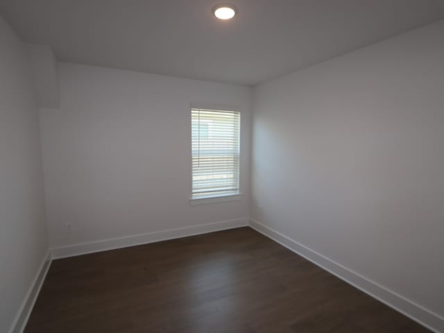 empty room with baseboards and dark wood-type flooring