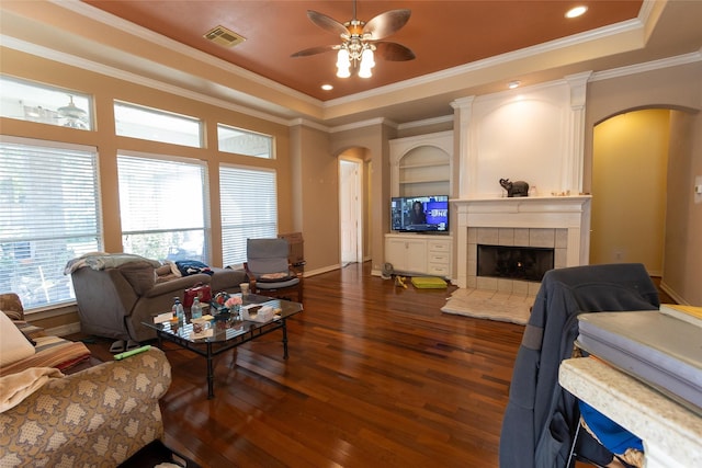 living room with dark hardwood / wood-style floors, ceiling fan, ornamental molding, and a tiled fireplace