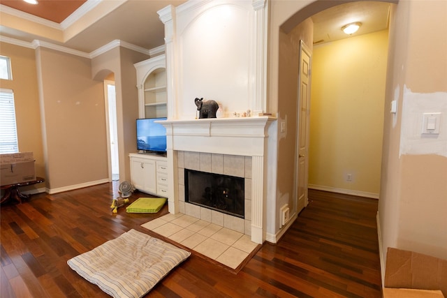 living room featuring a tiled fireplace, crown molding, and dark hardwood / wood-style floors