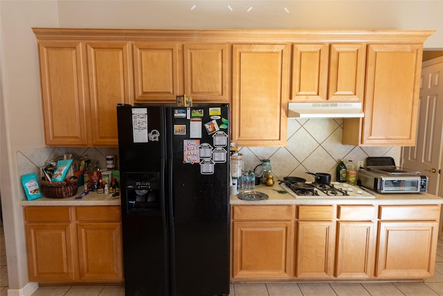 kitchen featuring decorative backsplash, black fridge with ice dispenser, light tile patterned floors, and white gas stovetop