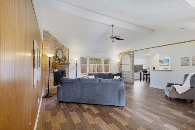 living room with wooden walls, dark hardwood / wood-style floors, ceiling fan, a fireplace, and beam ceiling