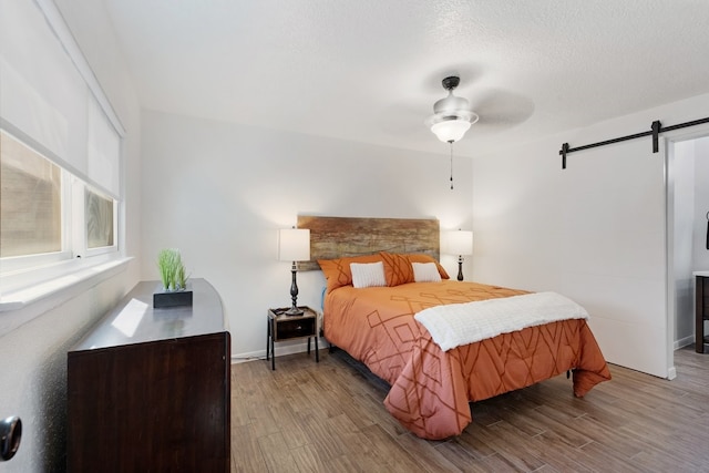 bedroom with wood-type flooring, a barn door, a textured ceiling, and ceiling fan