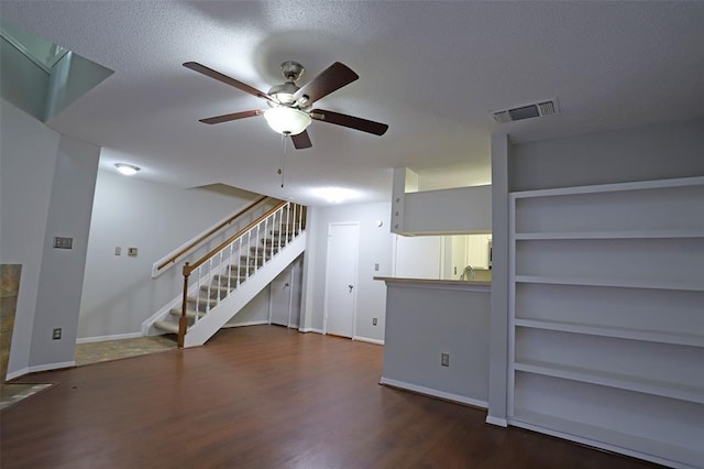 unfurnished living room with a textured ceiling, dark hardwood / wood-style flooring, built in features, and ceiling fan