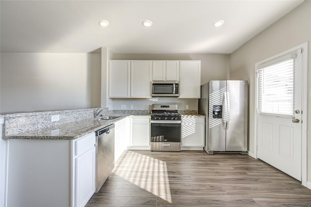 kitchen with light stone counters, stainless steel appliances, sink, wood-type flooring, and white cabinets