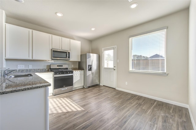 kitchen with light wood-type flooring, stainless steel appliances, sink, dark stone countertops, and white cabinetry