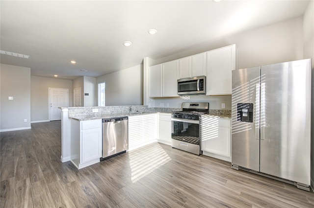 kitchen with white cabinetry, stainless steel appliances, light stone counters, kitchen peninsula, and wood-type flooring