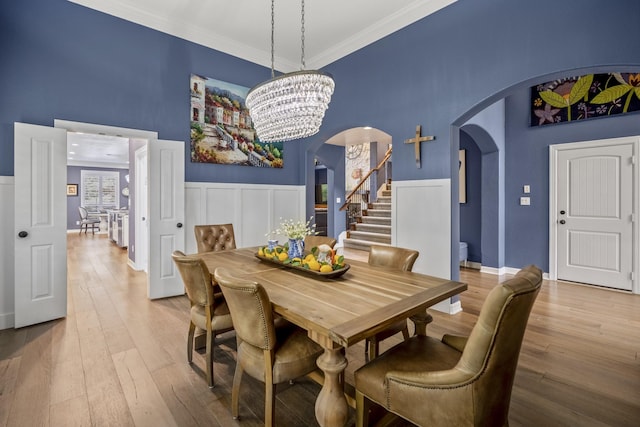 dining room featuring a chandelier, a towering ceiling, light hardwood / wood-style floors, and ornamental molding