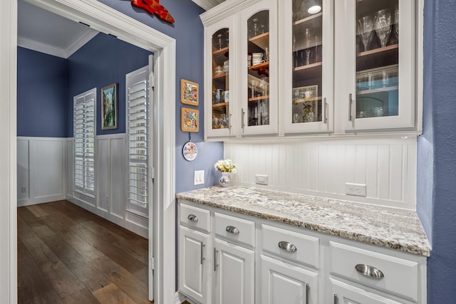 bar with light stone countertops, crown molding, white cabinetry, and dark wood-type flooring