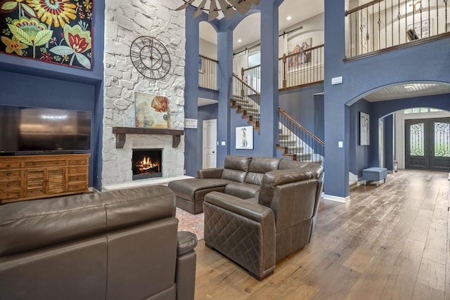 living room featuring a stone fireplace, hardwood / wood-style floors, a towering ceiling, and plenty of natural light