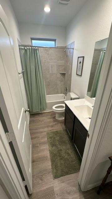 full bathroom with shower / bath combo with shower curtain, hardwood / wood-style floors, vanity, and toilet