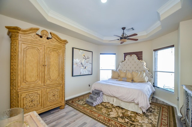 bedroom with a tray ceiling, ceiling fan, ornamental molding, and light wood-type flooring